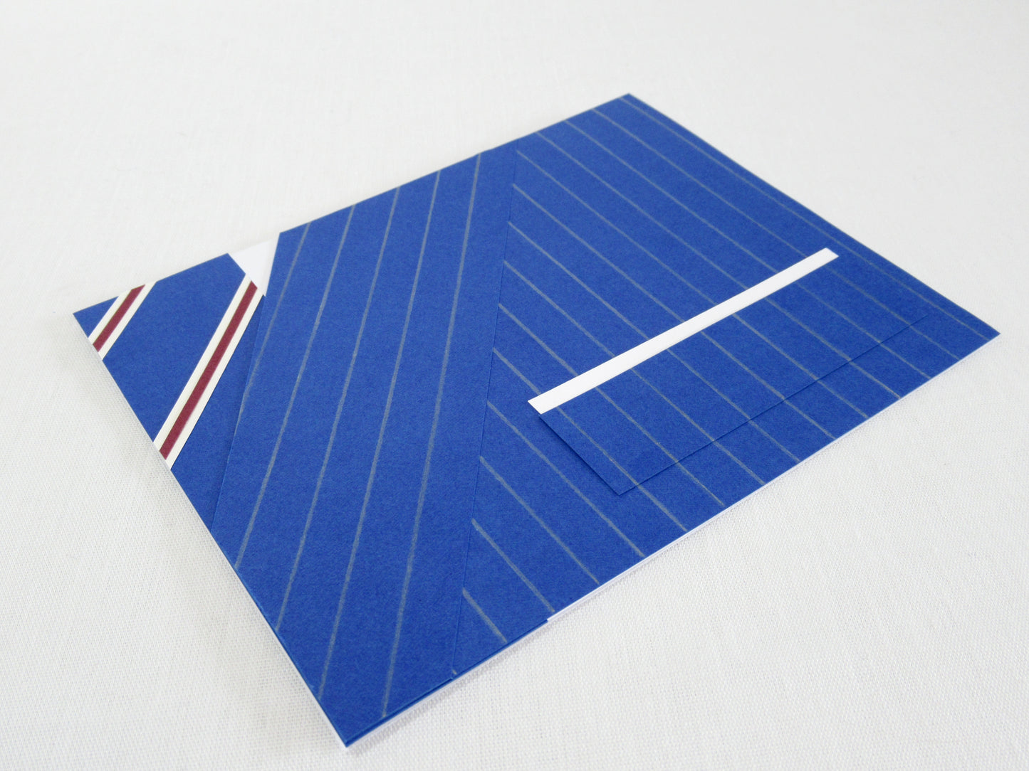 A card lays at an angle on a white desk. The front of the card looks like a portion of person's suit, blue pinstripes, white pocket square, and a blue striped tie. It's designed to look like an outfit worn by Harry Hart in the movie Kingsman: The Secret Service.