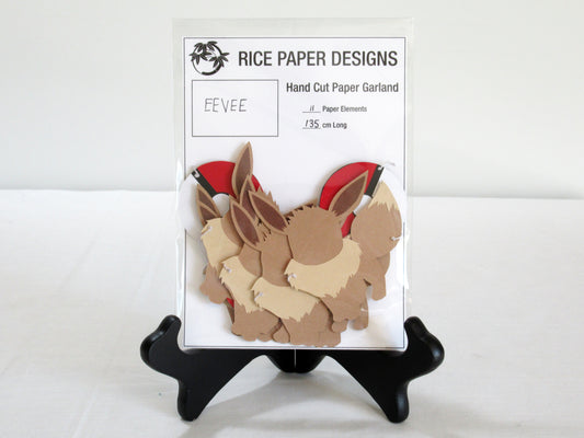 A garland with a series of paper eevees and pokeballs arranged in neat bundle inside a clear bag. There is a paper behind them showing the Rice Paper Designs logo, and information about the garland.
