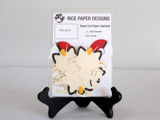 A garland with a series of paper meowths and pokeballs arranged in neat bundle inside a clear bag. There is a paper behind them showing the Rice Paper Designs logo, and information about the garland.