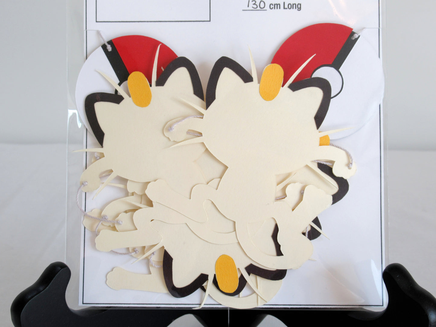 A close up of paper meowths and pokeballs on a string inside a clear bag.