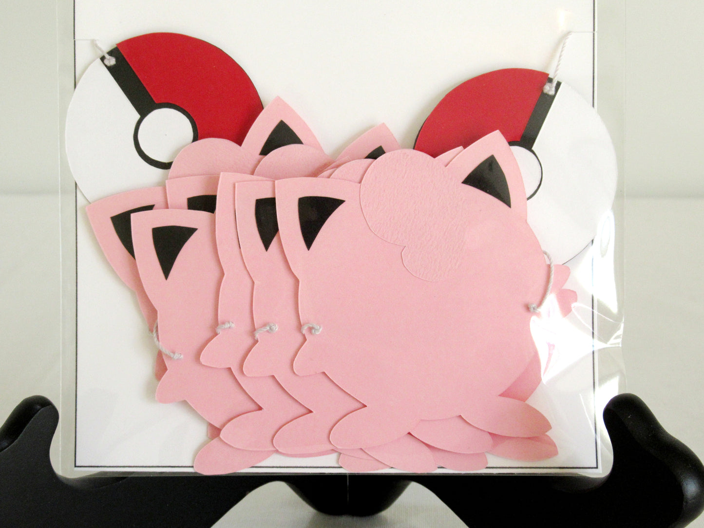 A close up of paper jigglypuffs and pokeballs on a string inside a clear bag.