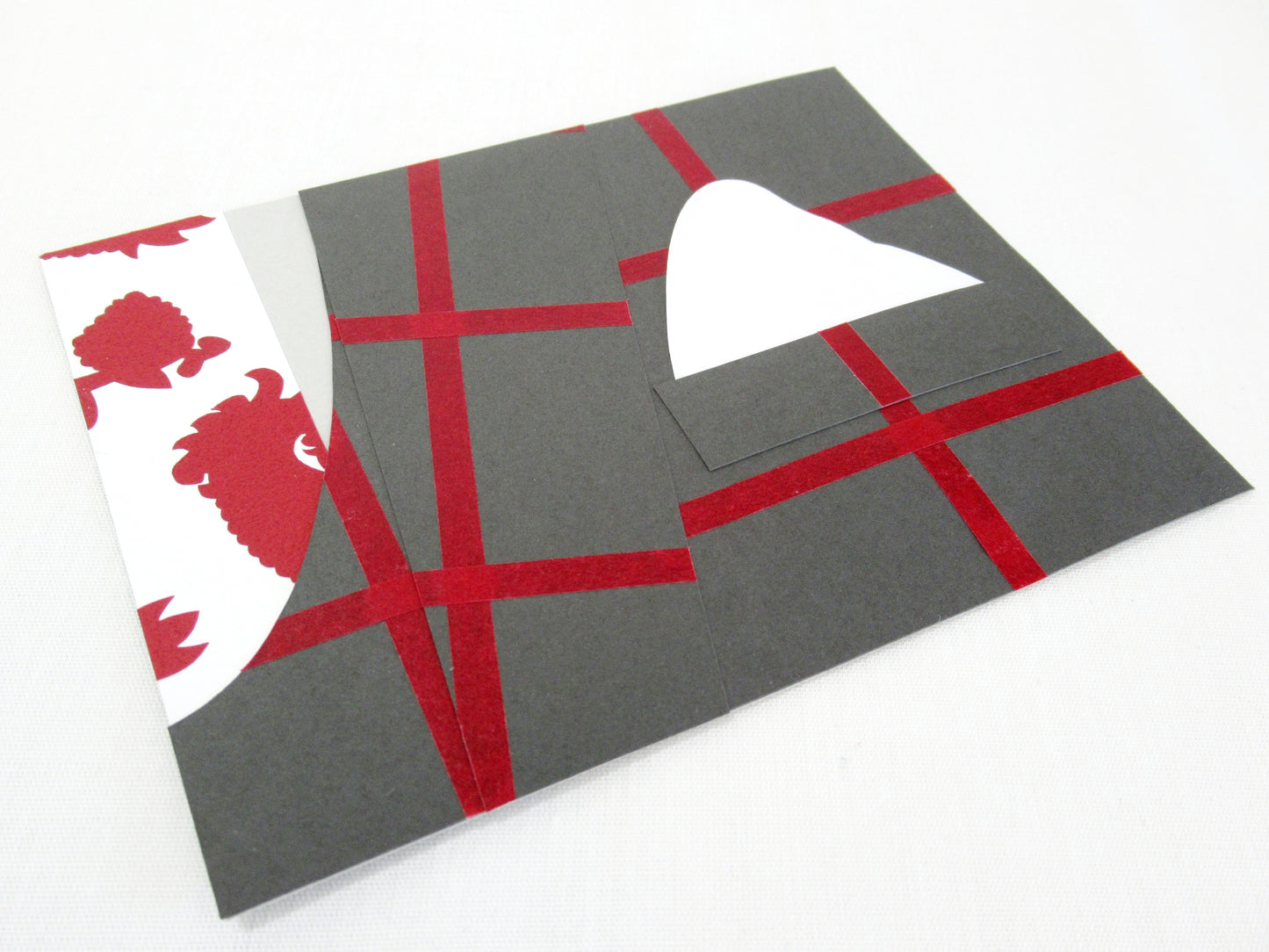 A card lays a white desk. The front of the card looks like a portion of person's suit, their tie and coat. The coat is dark grey with red stripes to form a check pattern. The tie is white with a red paisley pattern. Their is a white pocket square tucked into the pocket. The whole outfit is designed to look like one worn by Hannibal Lecter in the NBC show Hannibal.