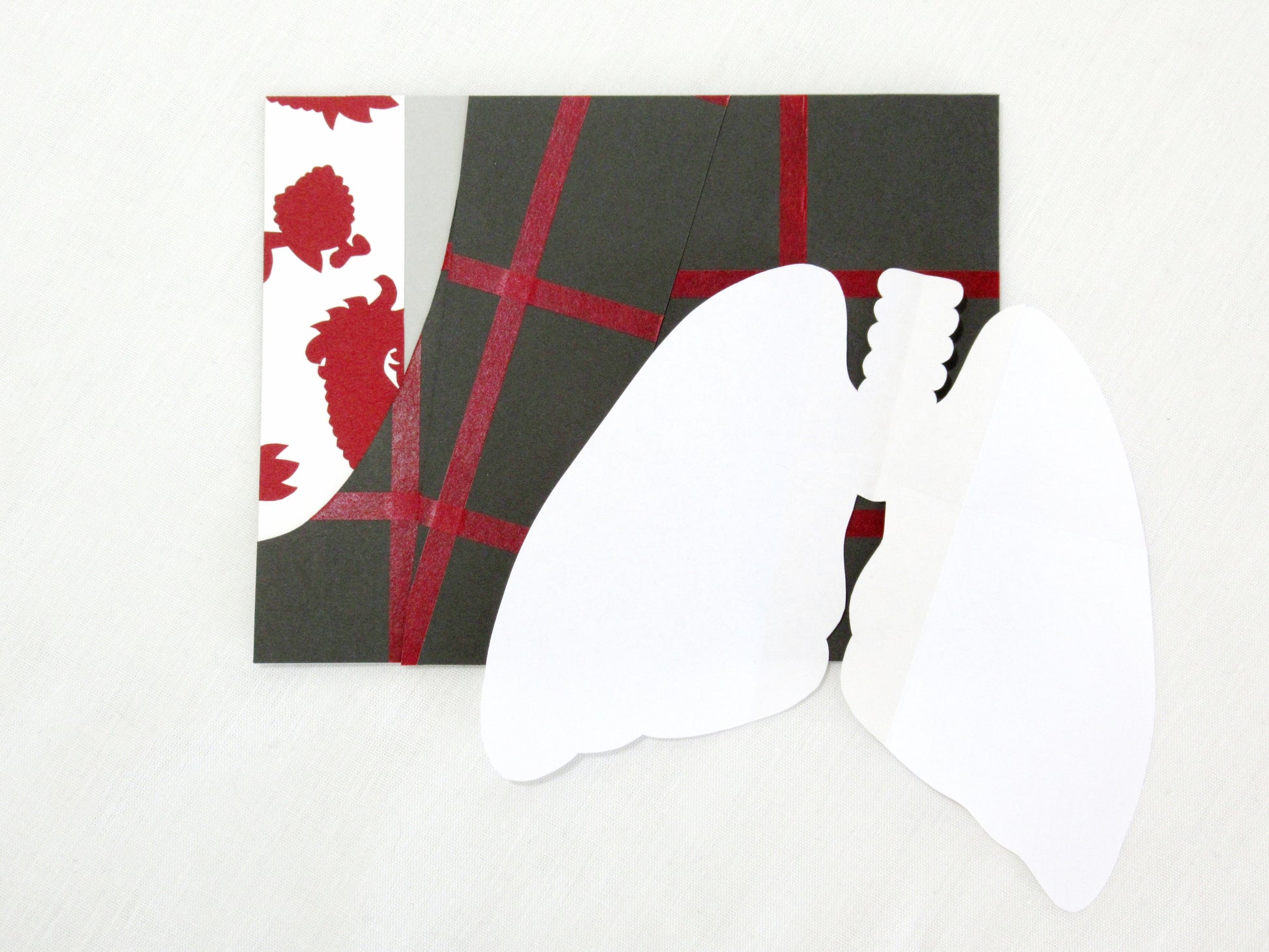 A card lays a white desk. The front of the card looks like a portion of person's suit, their tie and coat. The coat is dark grey with red stripes to form a check pattern. The tie is white with a red paisley pattern. The pocket square has been removed and opened up, showing it's been cut into the shape of a pair of lungs. The whole outfit is designed to look like one worn by Hannibal Lecter in the NBC show Hannibal.