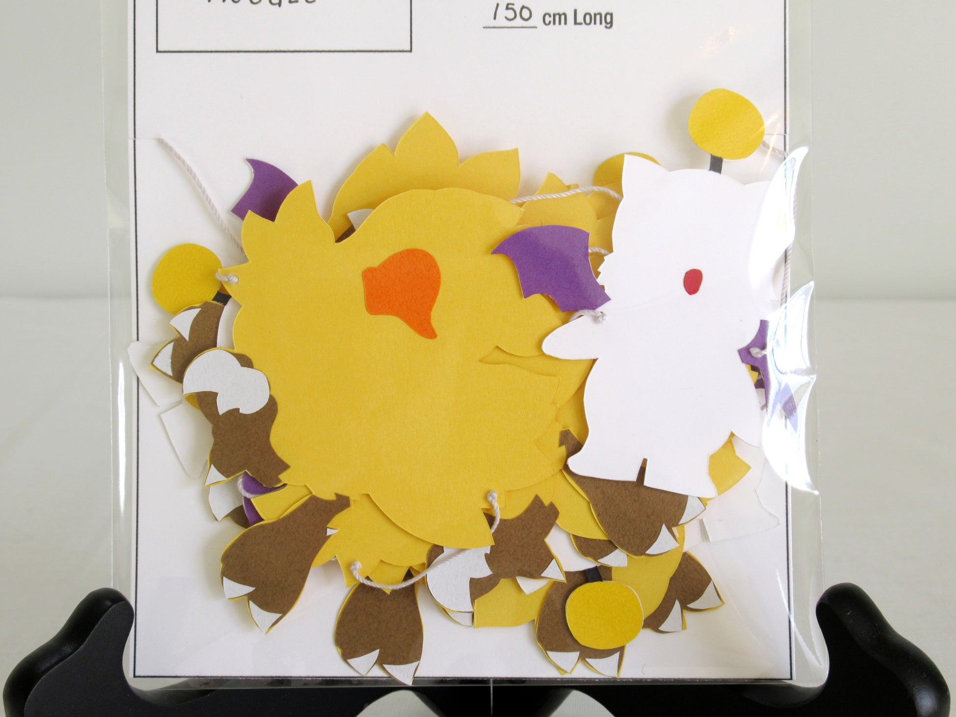 A close up of paper chocobo and moogles on a string inside a clear bag.