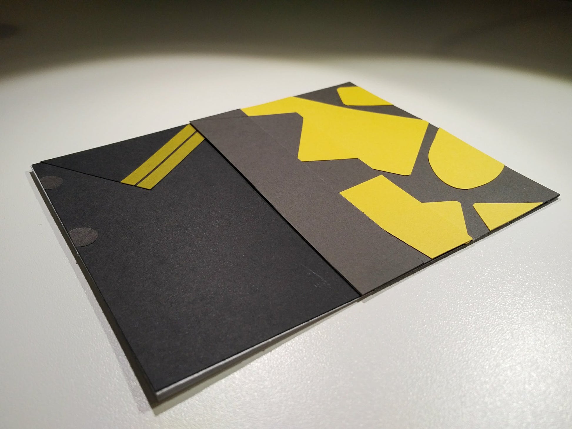 A card lays at an angle on a white desk. The front of the card looks like a portion of person's shirt, black with yellow details, designed to look like an outfit worn by Eggsy Unwin in the movie Kingsman: The Secret Service.