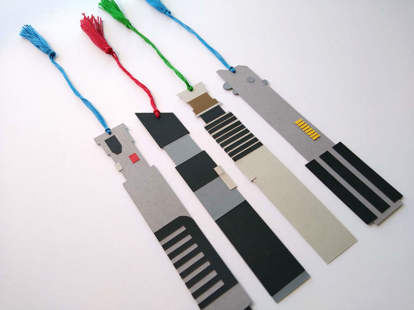 Four bookmarks with tassels stretched out lay on a white background. Each bookmark is designed to look like a light saber from Star Wars, with the light portion represented by a colored tassel.