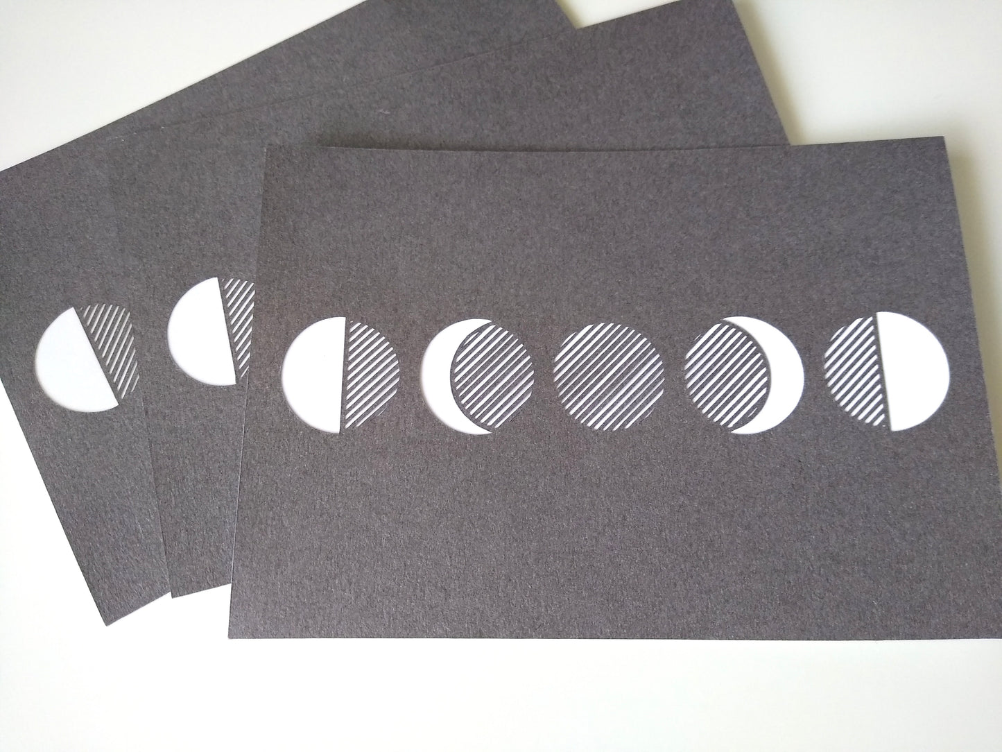 A close up of three postcards, metallic grey and with five moon phases on them.