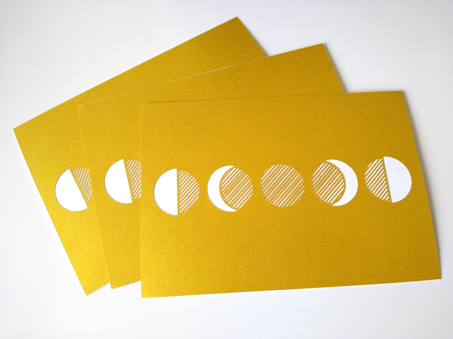 Close up of three postcards, gold and with five moon phases on them.