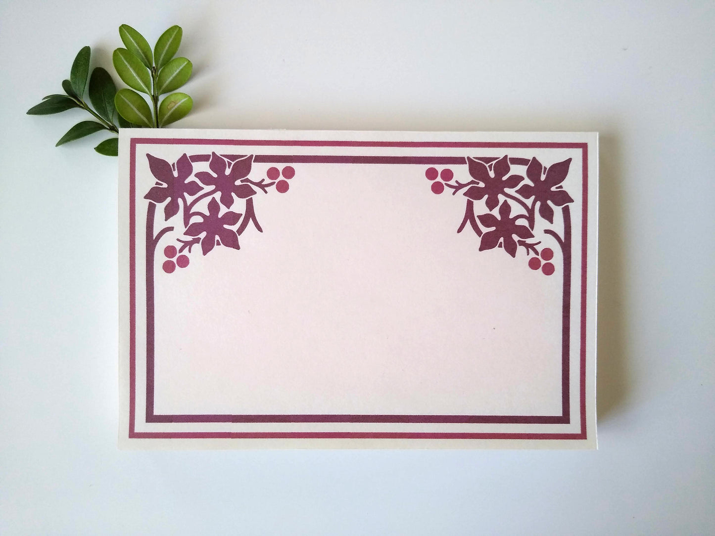 A single notepad with a stylized maple leaf design in both upper corners. There is a double line border around the whole notepad. Two small sprigs of leaves rest under the upper left hand corner.