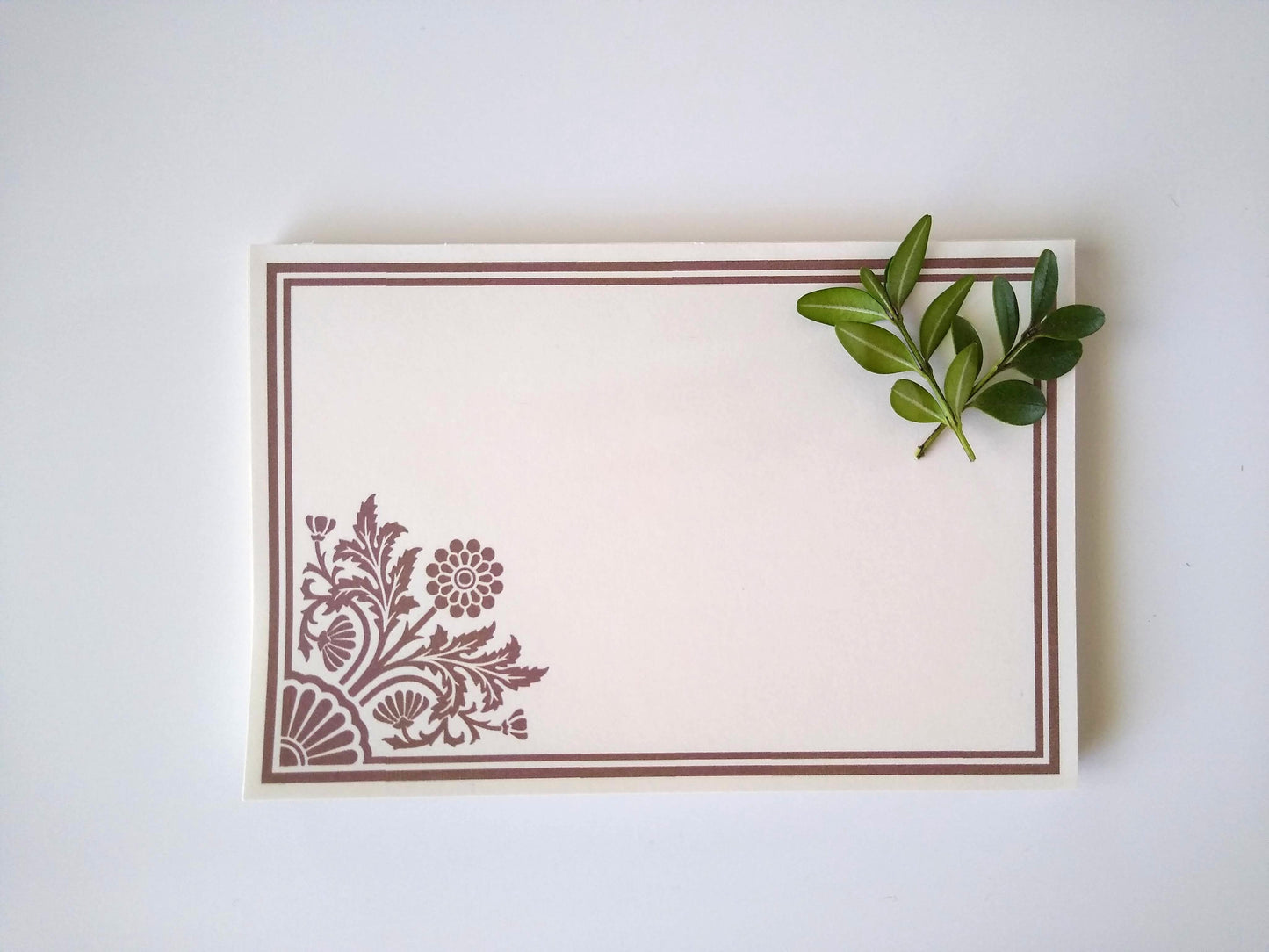 Single notepad with a stylized dahlia design in the lower left corner. There is a double line border around the whole notepad. Two small sprigs of leaves rest on the upper right hand corner.