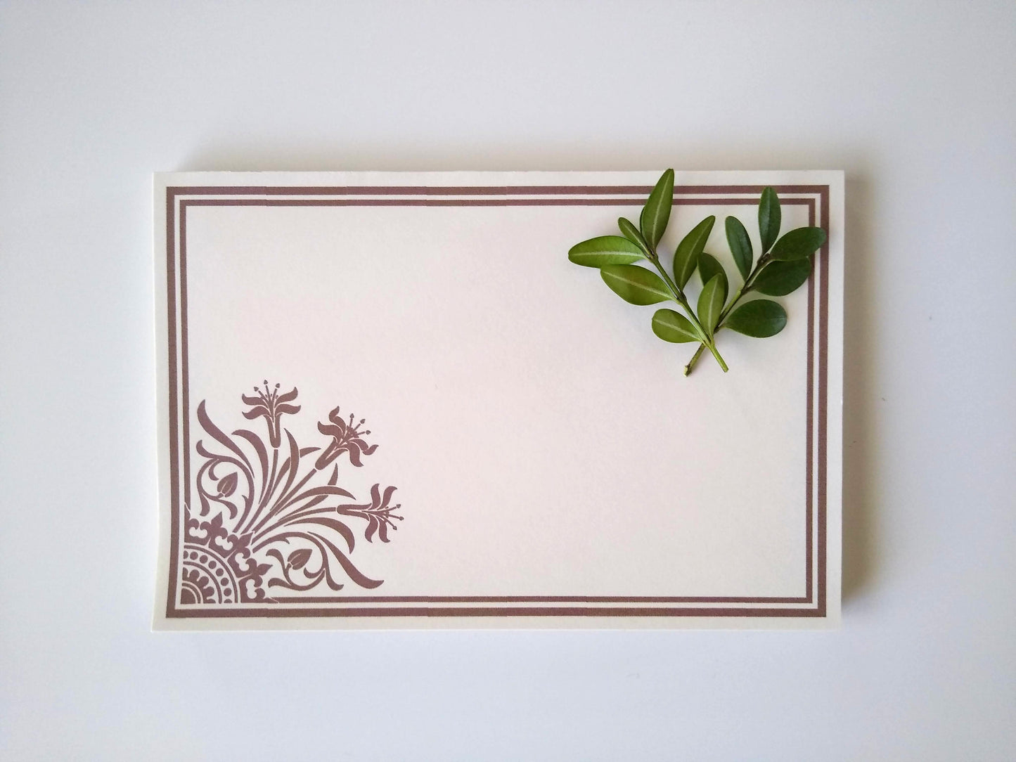 Single notepad with a stylized lily design in the lower left corner. There is a double line border around the whole notepad. Two small sprigs of leaves rest on the upper right hand corner.